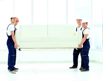 happy male movers in uniform carrying white sofa